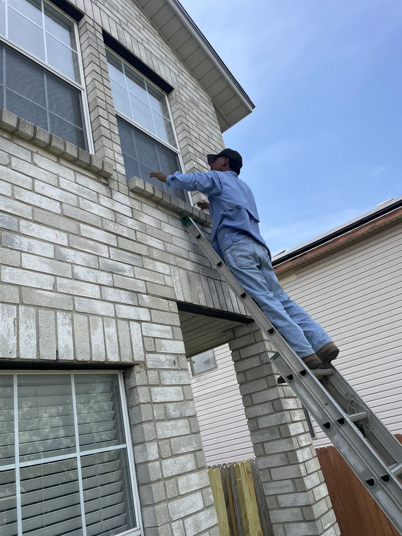 JP, owner of M&J Solar Screens, on a ladder fitting a screen to a second-story window